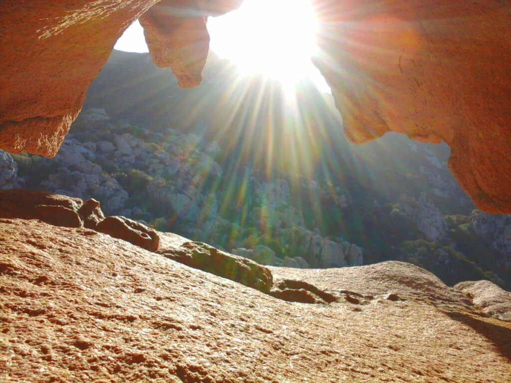 Sonnenstrahlen fallen durch eine schmale Felsöffnung in der Granitlandschaft Sardiniens.