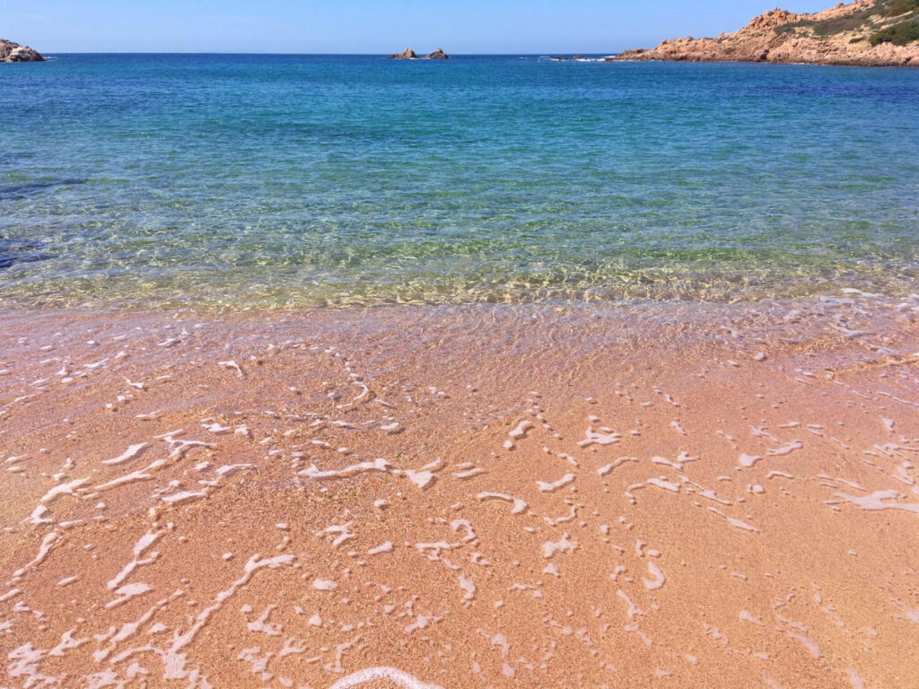 Feiner Sandstrand mit klarem Wasser und sanften Wellen.