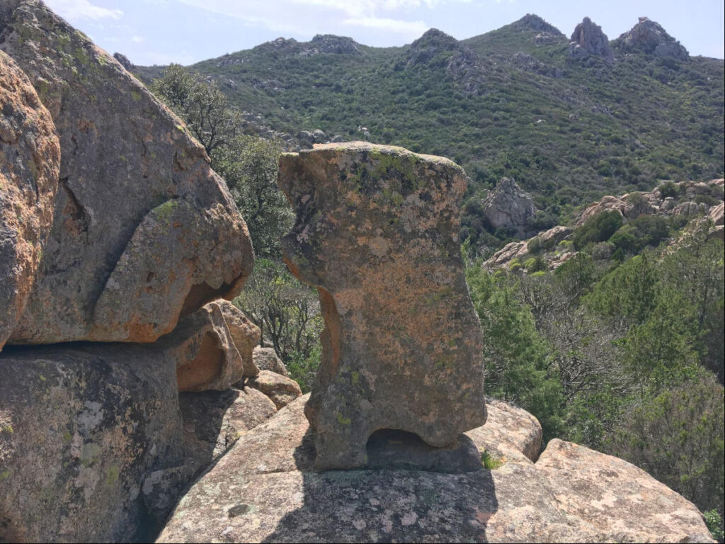 Zwei aufragende Granitsteine mit Blick in die weite Hügellandschaft Sardiniens.
